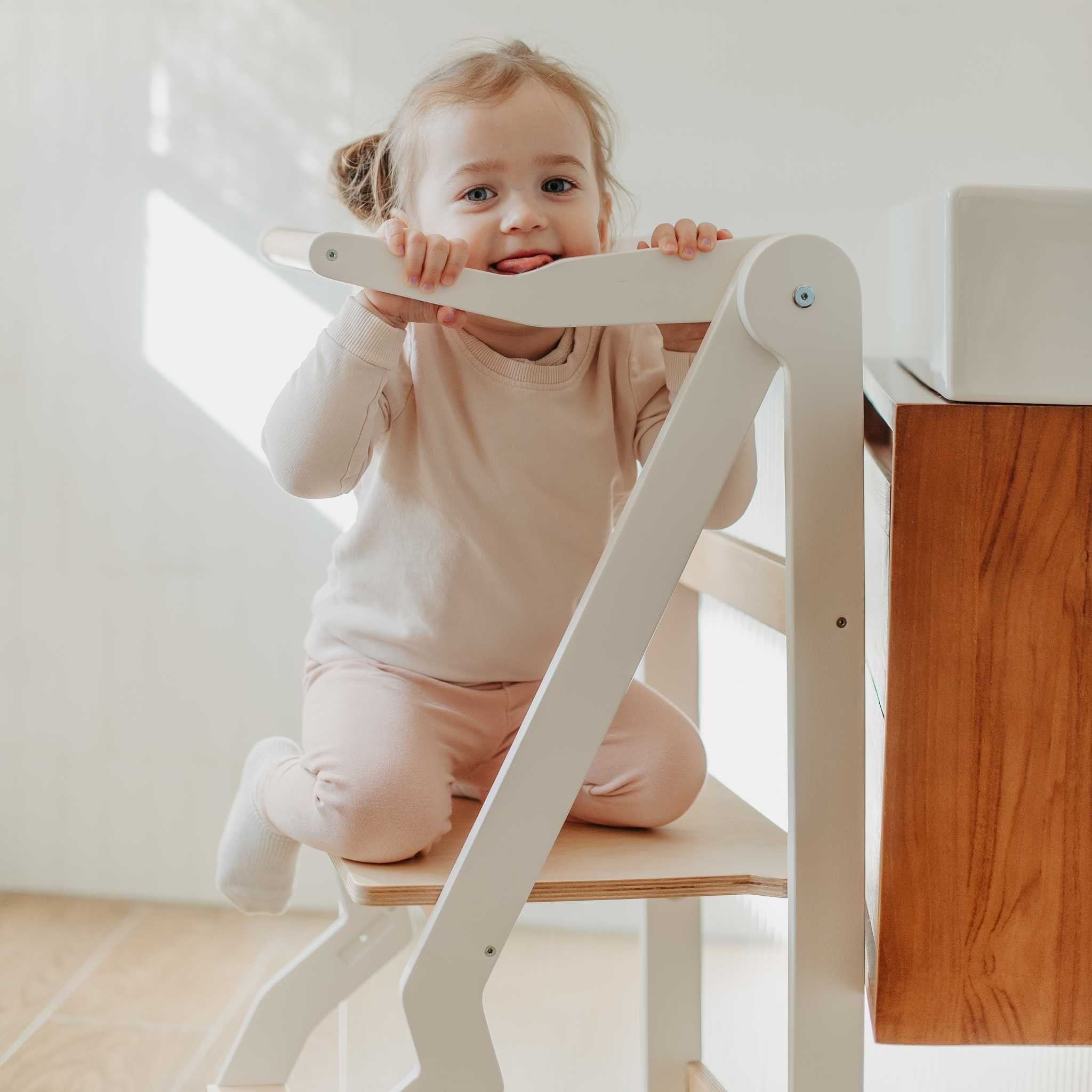 Lapsi kiipeilee lasten taitettavalla apujakkaralla. Apujakkara on taitettava ja valkoinen